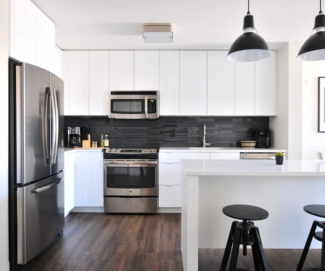 White flat-panel kitchen with a dark tile backsplash, black pendant lights and dark wood flooring