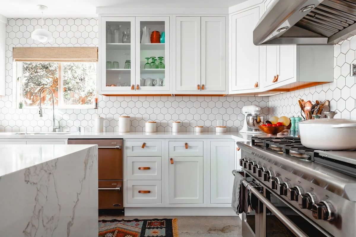 Bright kitchen with painted white shaker cabinets, leather pulls and a professional range